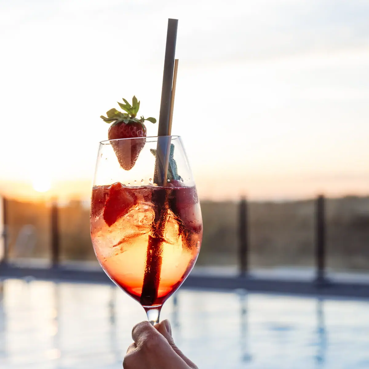 Drink Een hand houdt een drankje met aardbeien vast, op de achtergrond is een zwembad te zien.