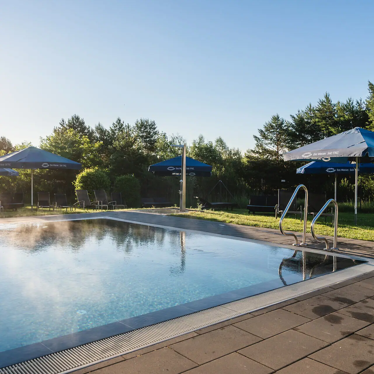 Buitenzwembad aja Bad Saarow Een buitenzwembad met parasols en gras rondom.