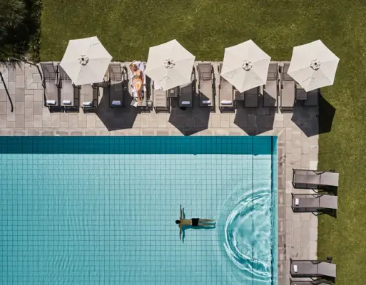 Persoon zwemt in een zwembad met parasols en gras.