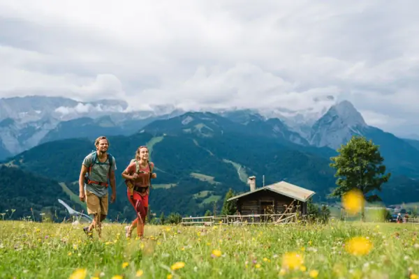 Wandelen in Garmisch-Partenkirchen Een man en een vrouw lopen door een veld met bergen op de achtergrond.