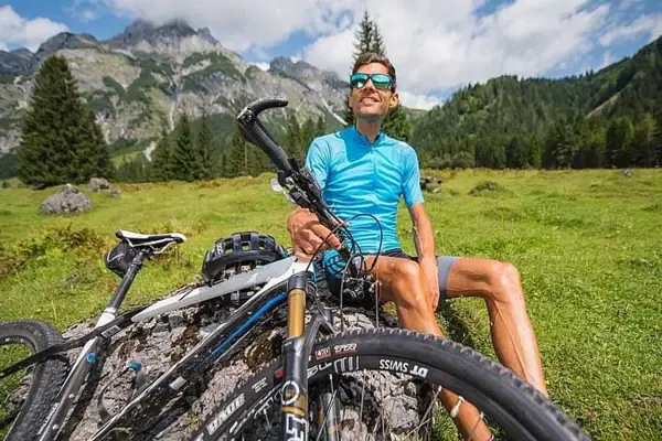 Man zittend op een rots met zijn fiets voor de achtergrond van een berg.