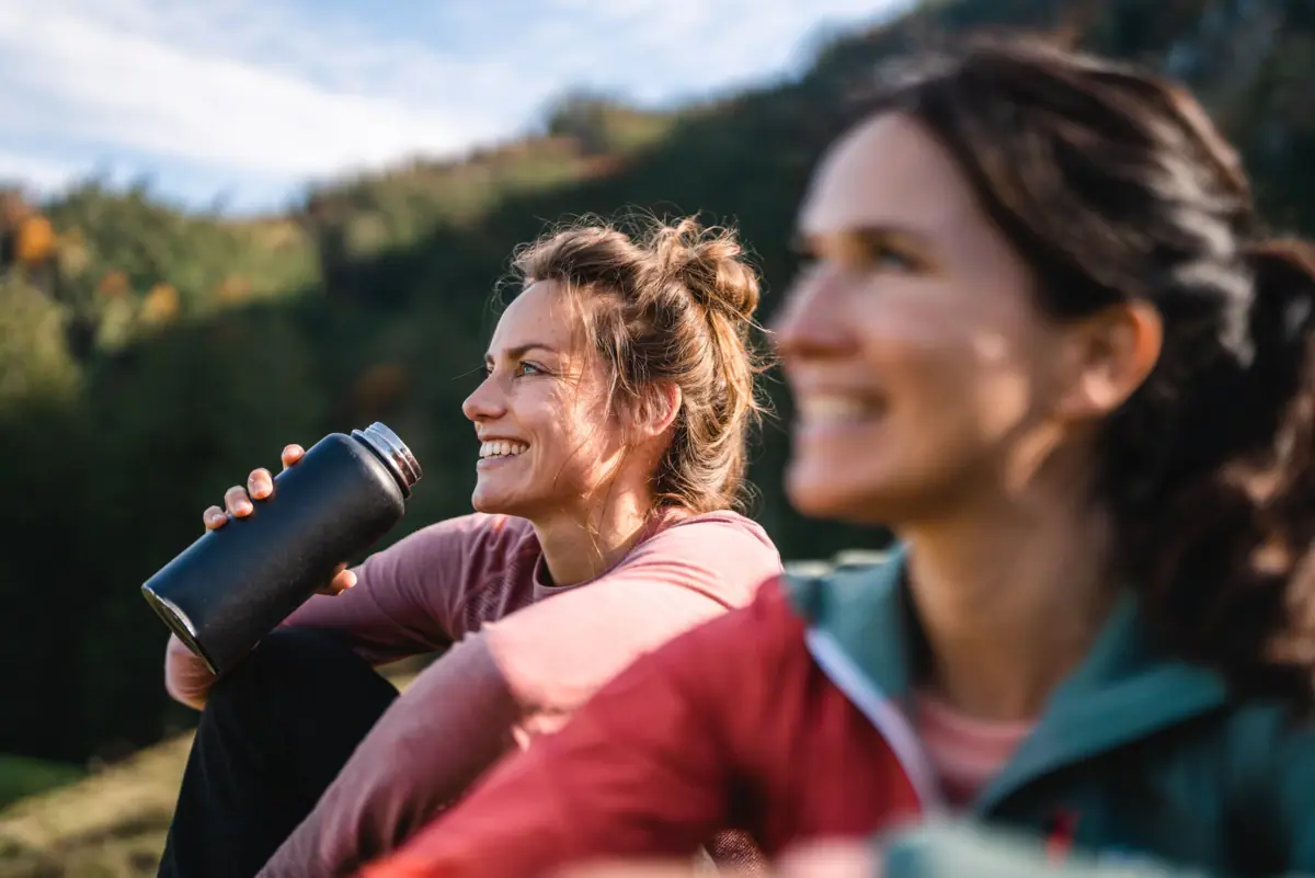 Twee vrouwen zitten naast elkaar in de open lucht en glimlachen.