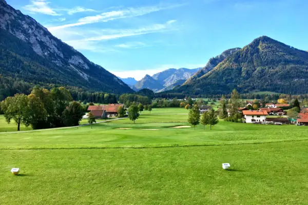 Golfbaan Ruhpolding Groot groen veld met bomen en bergen op de achtergrond.