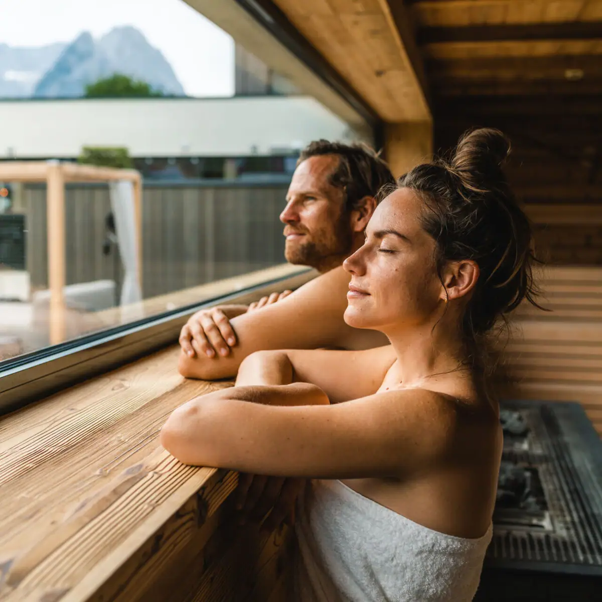 Paar in de sauna Een man en een vrouw in trouwkleding leunen tegen een raam.