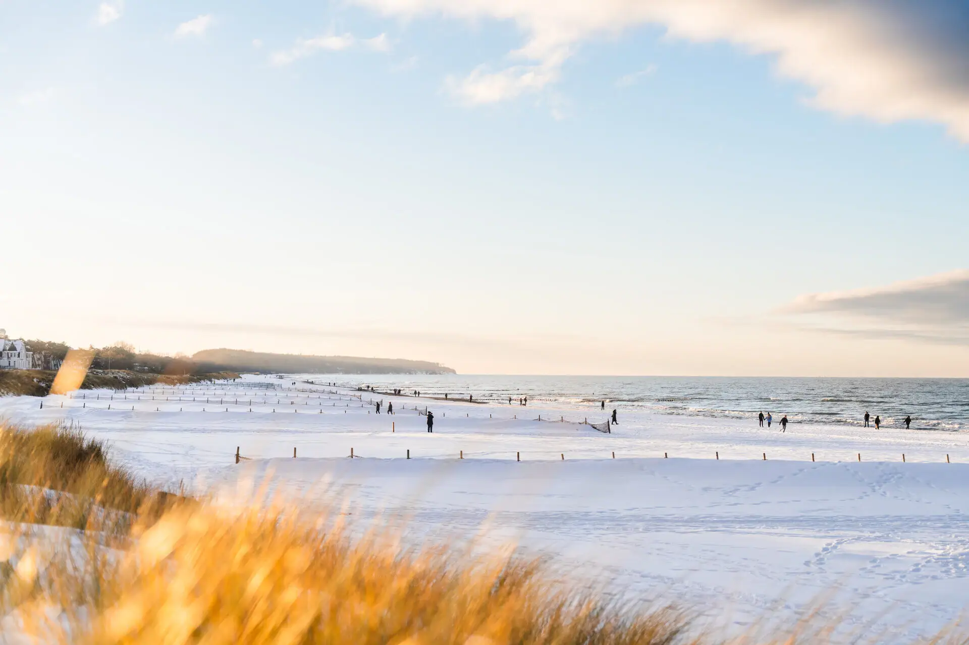 Het strand in Warnemünde is bedekt met sneeuw. De duinen stralen in de zon en mensen lopen in warme kleren over het strand.