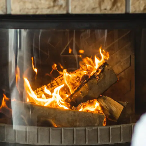 Een persoon houdt een glas wijn vast voor een open haard.