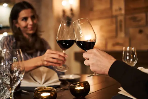 Een man en een vrouw klinken glazen wijn aan een tafel.