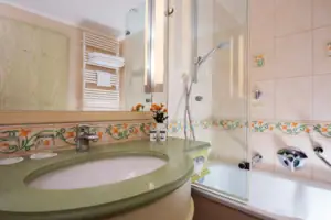 Junior tweepersoonskamer Landside met balkon Badkamer met wastafel en bad, tegels op de muren, kraan en spiegel.