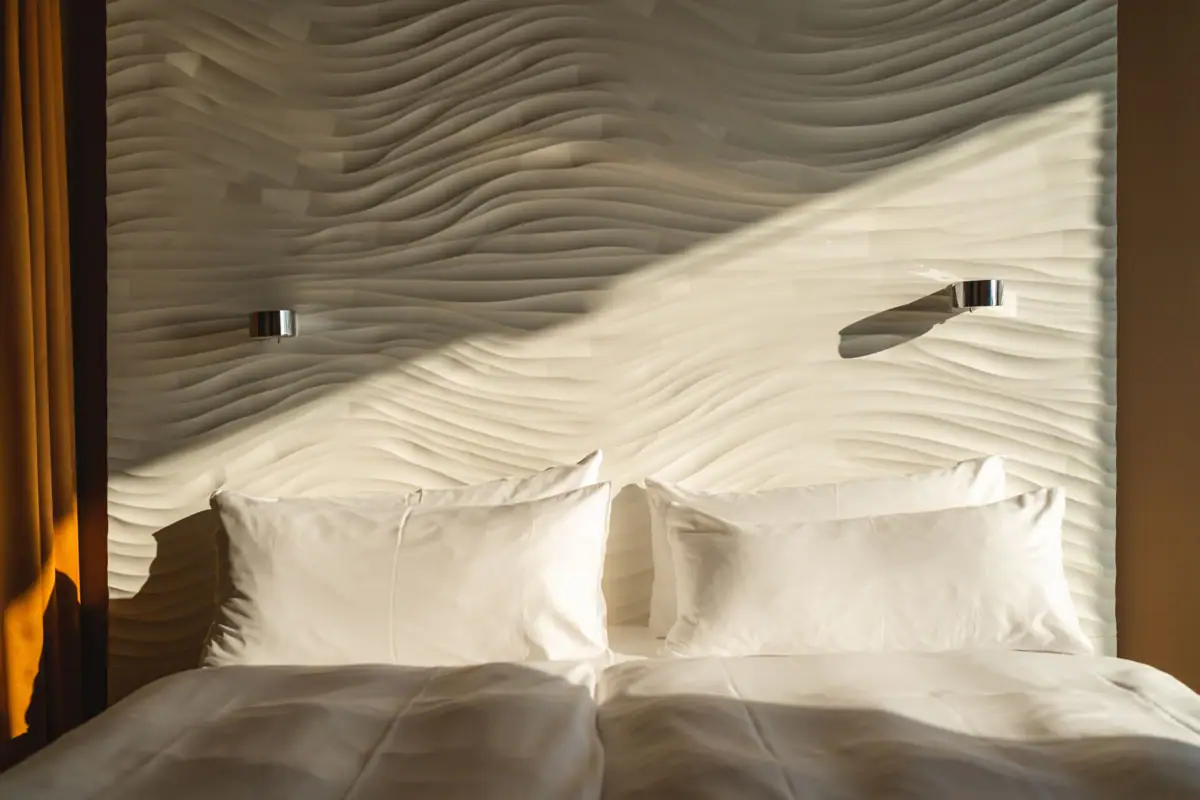 Kamers in het aja Warnemünde Een bed met kussens voor een verlichte muur.