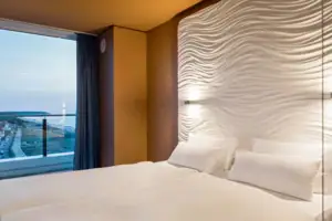 Suite bij de aja Warnemünde Bed met witte lakens voor een muur met een raam met uitzicht op zee