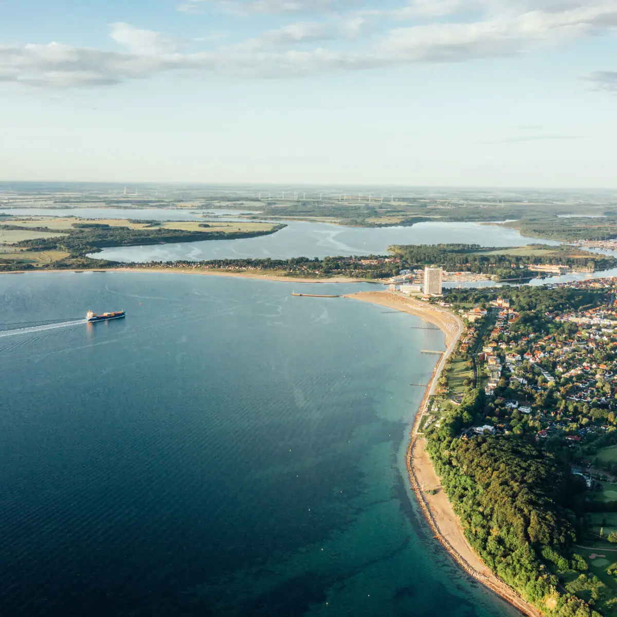Baai van Lübeck Luchtfoto van een waterlichaam en een kustplaats onder een bewolkte hemel.