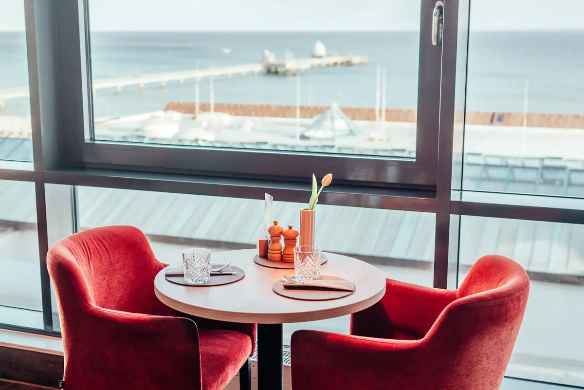 JEDERMANNS Restaurant Grömitz Een tafel met rode stoelen en uitzicht op de Oostzee