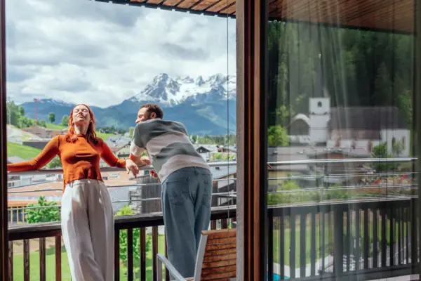 Een man en een vrouw staan op een veranda en kijken naar de bergen.