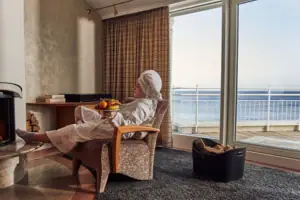 Een vrouw in een witte badjas zit in een stoel met een schaal fruit op haar schoot.