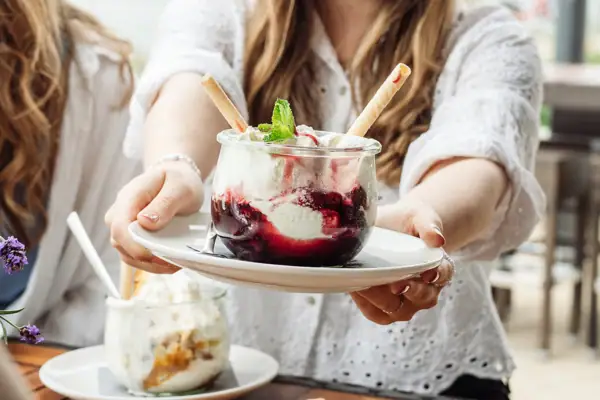 Een vrouw houdt een bord vast met een sundae met vanille-ijs en kersen.