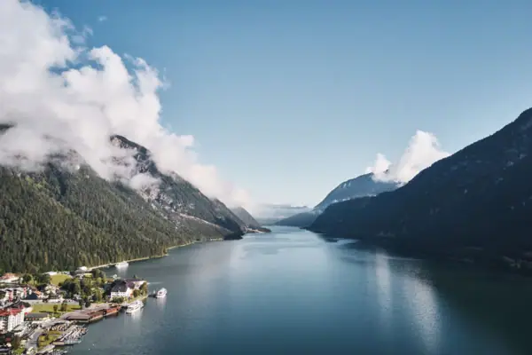 Achensee Meer Een waterlichaam met een huis en bergen op de achtergrond.