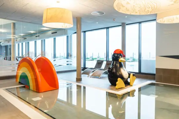 Een speelgoedpinguïn in een kamer met een glijbaan en een regenboog.
