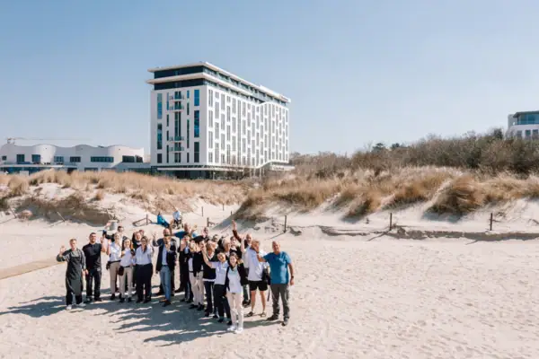 Team van de aja Warnemünde Een groep mensen van het hotelteam poseert voor een foto voor het aja Warnemünde gebouw.