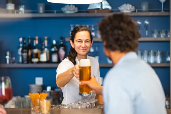 Een vrouw houdt een glas bier vast aan de bar en overhandigt het aan een gast.