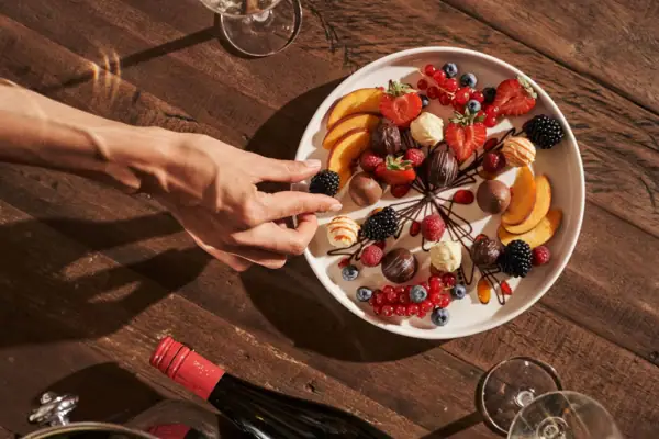 Een hand reikt naar een bord fruit.