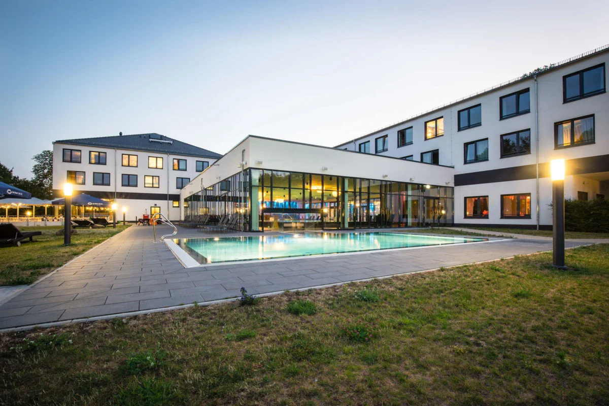 aja Bad Saarow Een hotelgebouw met een zwembad en een grasveld.