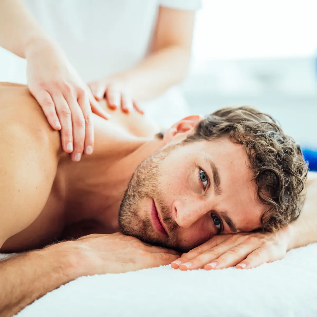 Een man ligt op een massagetafel en laat zijn nek masseren.