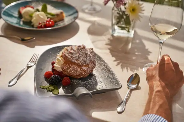 Een bord dessert en bessen naast een glas wijn.