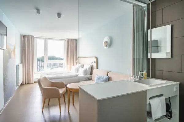 aja Travemünde Zimmer Ein modernes, helles Hotelzimmer mit einem Bett und einem Sofa.