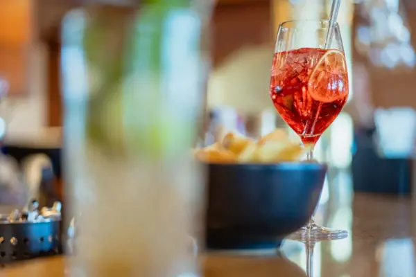 Cocktail Een glas rode vloeistof met een rietje naast een schaaltje chips.