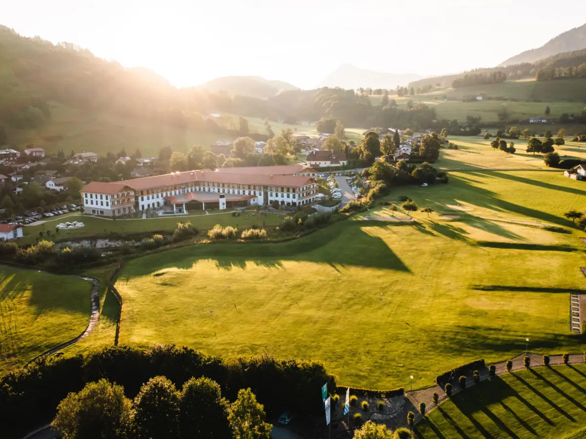 Groen veld met een gebouw en bomen op de achtergrond.