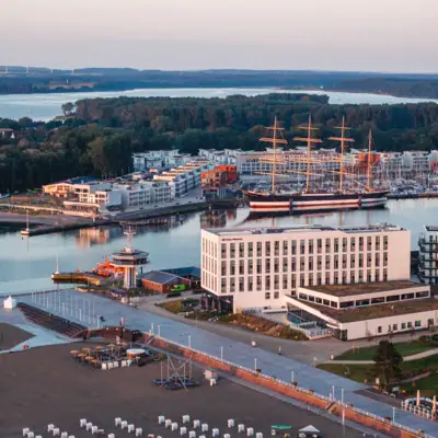 aja Travemünde Das aja Travemünde direkt am Wasser gelegen mit Booten und Gebäuden im Hintergrund.