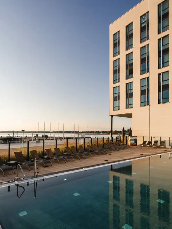 Een zwembad met ligstoelen en een gebouw op de achtergrond.