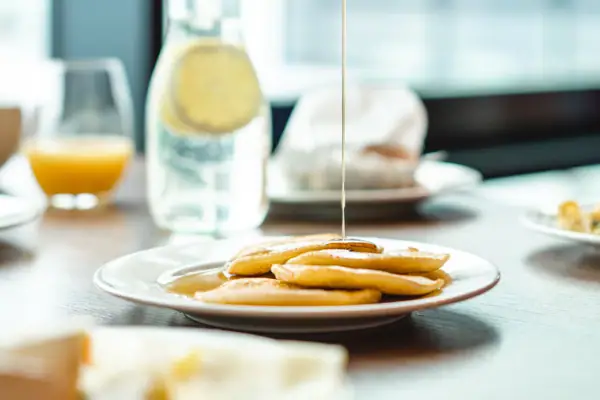 Eén persoon giet stroop op een bord pannenkoeken.