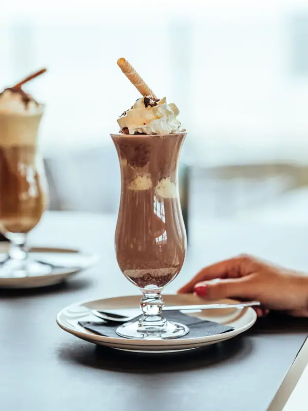 Een glas chocolademilkshake met slagroom en wafels.