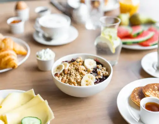 Een kom muesli met bananen en pannenkoeken op tafel.