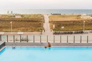Ein Mann und eine Frau am Rand eines Außenpools mit Blick auf den Strand und die Ostsee.