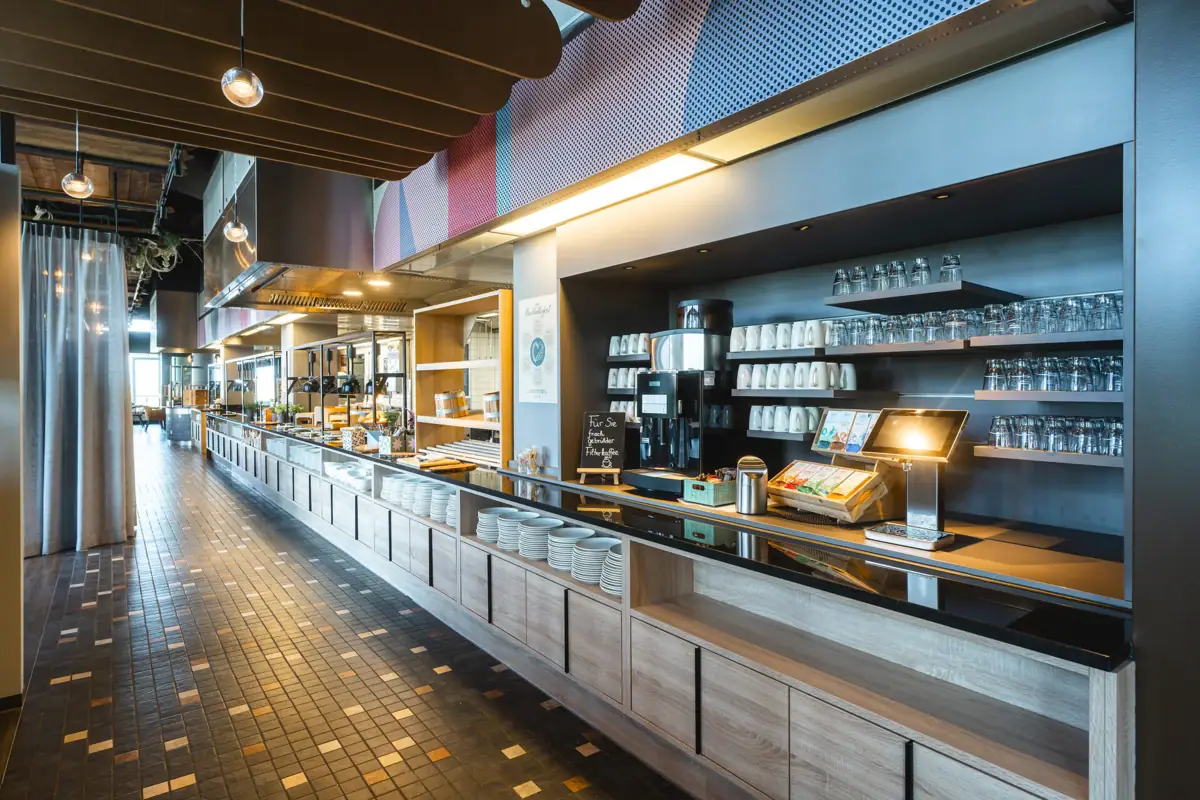 Restaurant bij aja Warnemünde Het buffetrestaurant met toonbanken en planken vol serviesgoed.