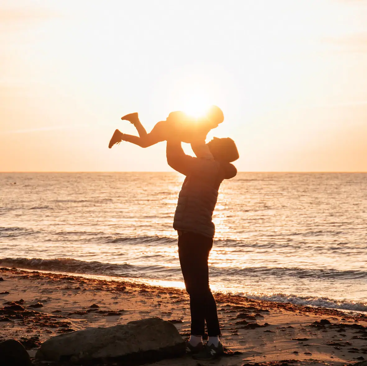 Een vrouw houdt een baby vast op het strand.