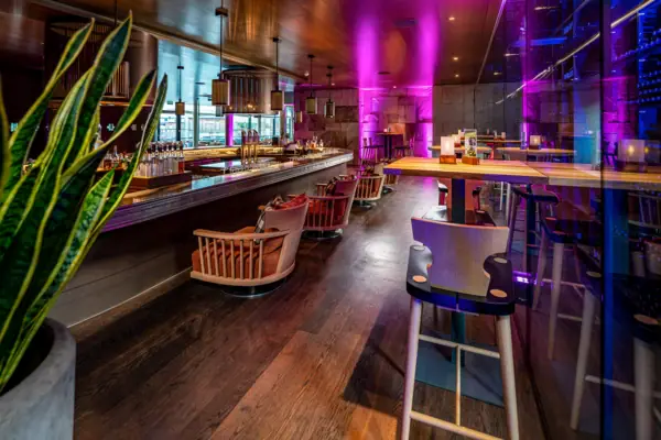 Een bar met stoelen en tafels in een ruimte met paarse verlichting.