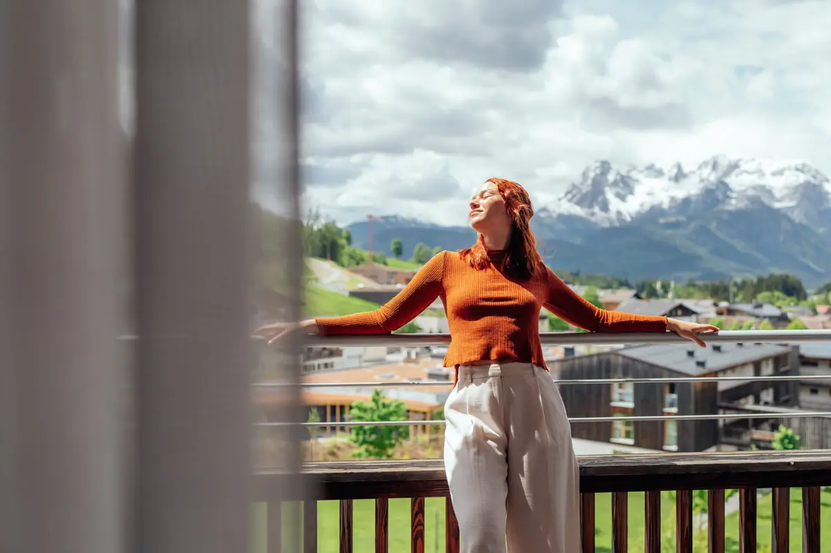 Een vrouw staat met uitgestrekte armen op een balkon.