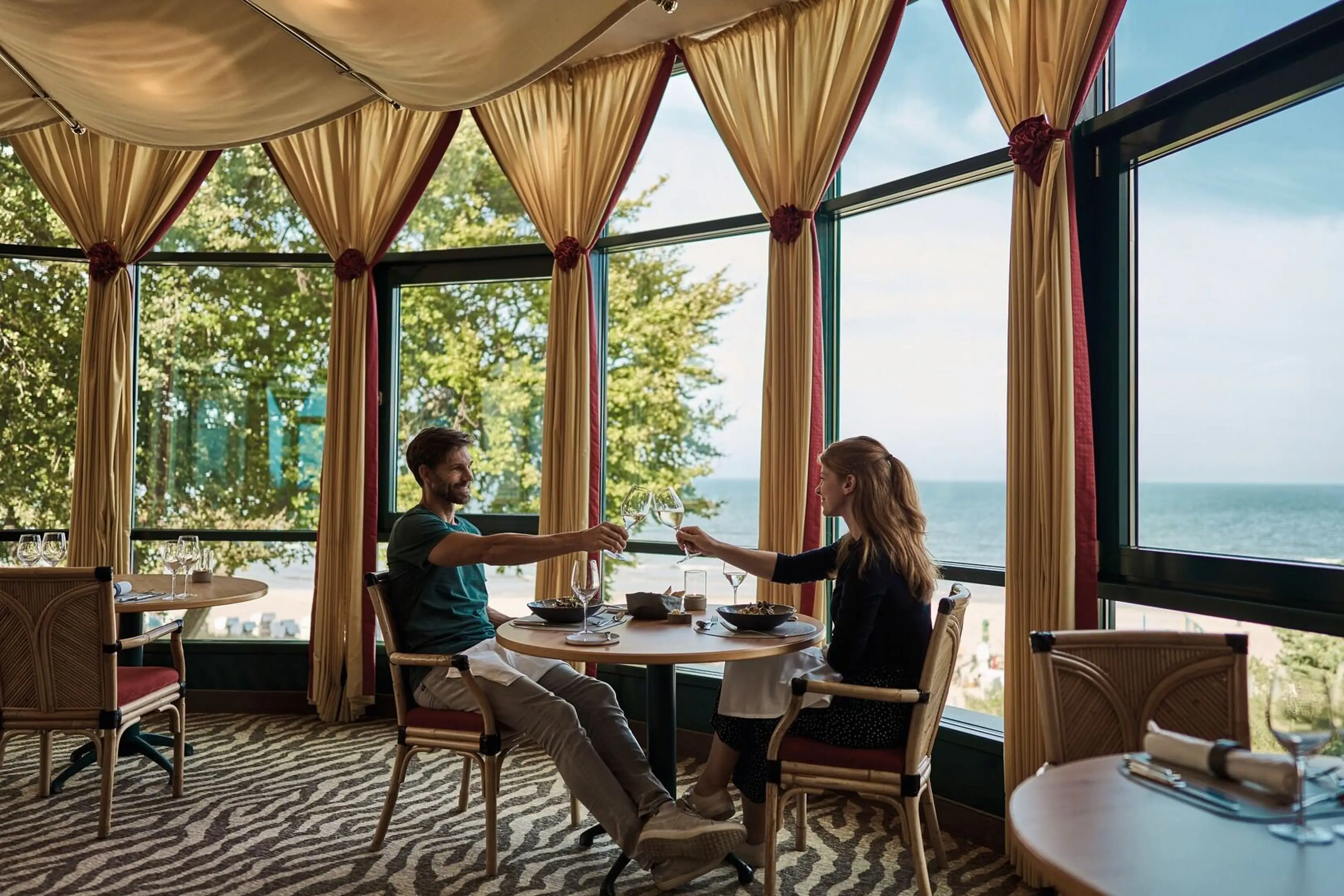 Een man en een vrouw zitten aan een tafel met eten voor een groot raam.