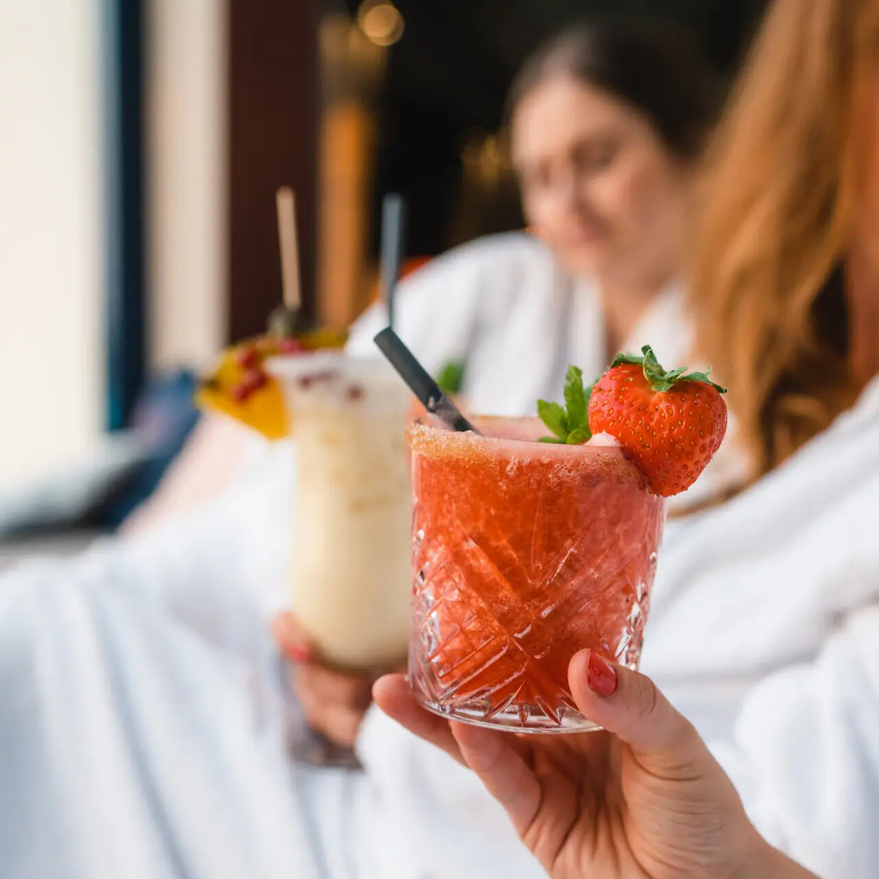 Cocktails Hand houdt twee drankjes vast, één met aardbeiengarnering.