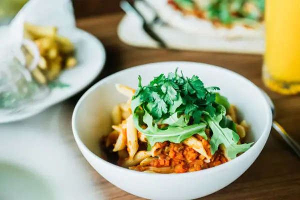 Een kom pasta met saus en groene ingrediënten.