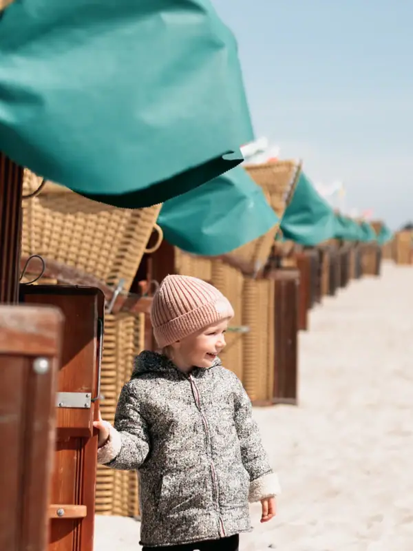 Een kind staat in het zand naast een rij strandhutten.