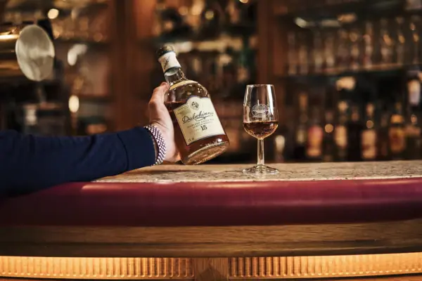 Naast een wijnglas houdt iemand een fles alcohol vast.