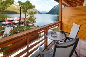 Tweepersoonskamer balkon Een balkon met tafel en stoelen met uitzicht op een meer.