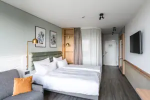 Kamers in het aja Warnemünde Hotelkamer met tweepersoonsbed, voorzien van kussens en beddengoed. TV aan de muur en bank naast het bed.