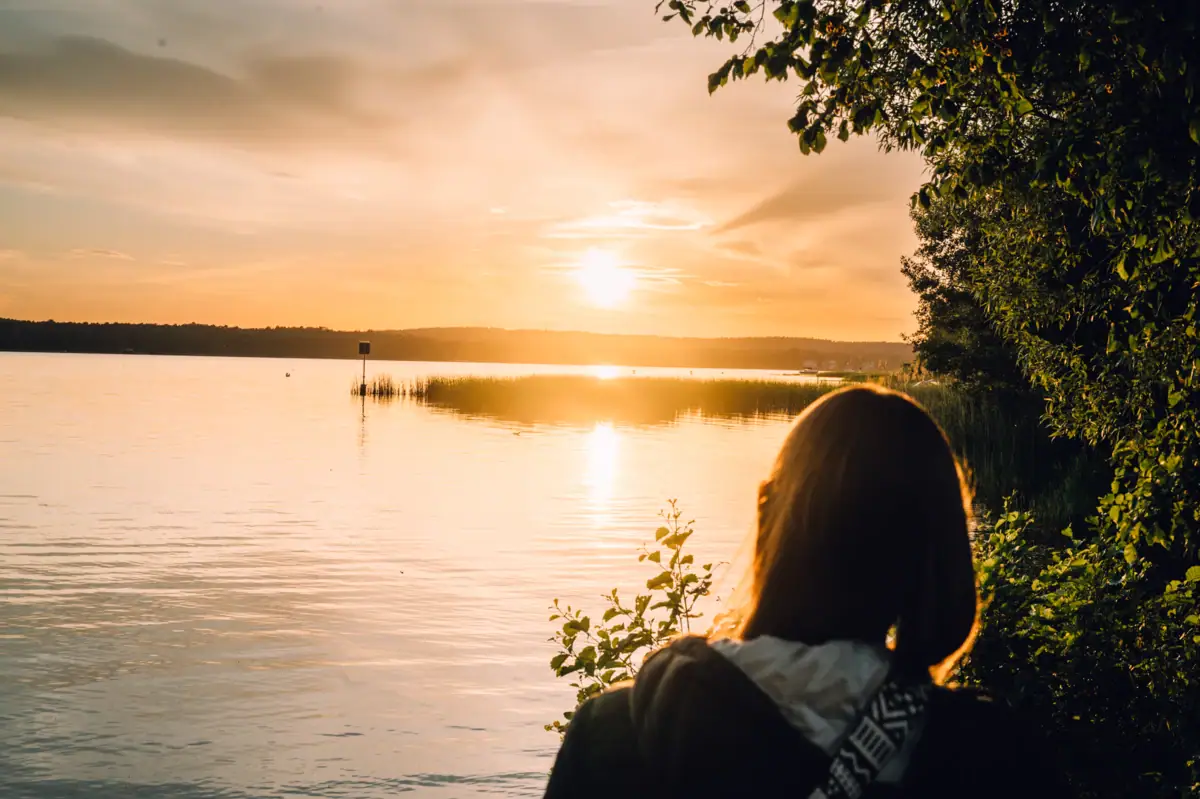 Een vrouw kijkt naar de zonsondergang boven het water.