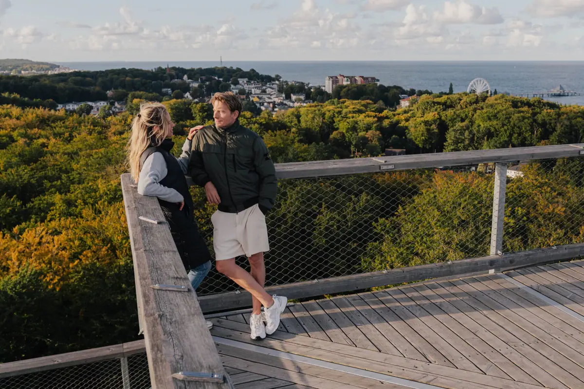 Een man en een vrouw staan op een houten vlonder met uitzicht op een bos.