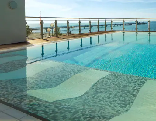 Uitzicht over het rustige water van het buitenzwembad van Grömitzer Welle naar de Baltische Zee op de achtergrond, dat van het buitengedeelte van het zwembad wordt gescheiden door een glazen hek.